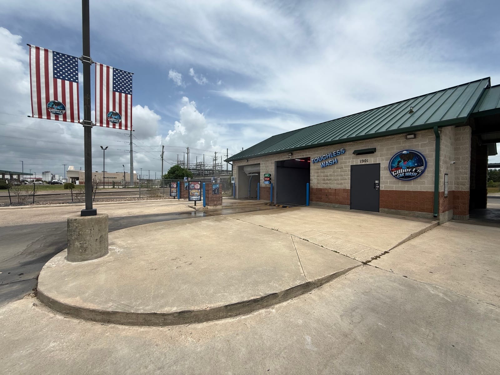 Touchless wash building, pay stations, and American flags at Gilbert's Car Wash Victoria on a sunny day.